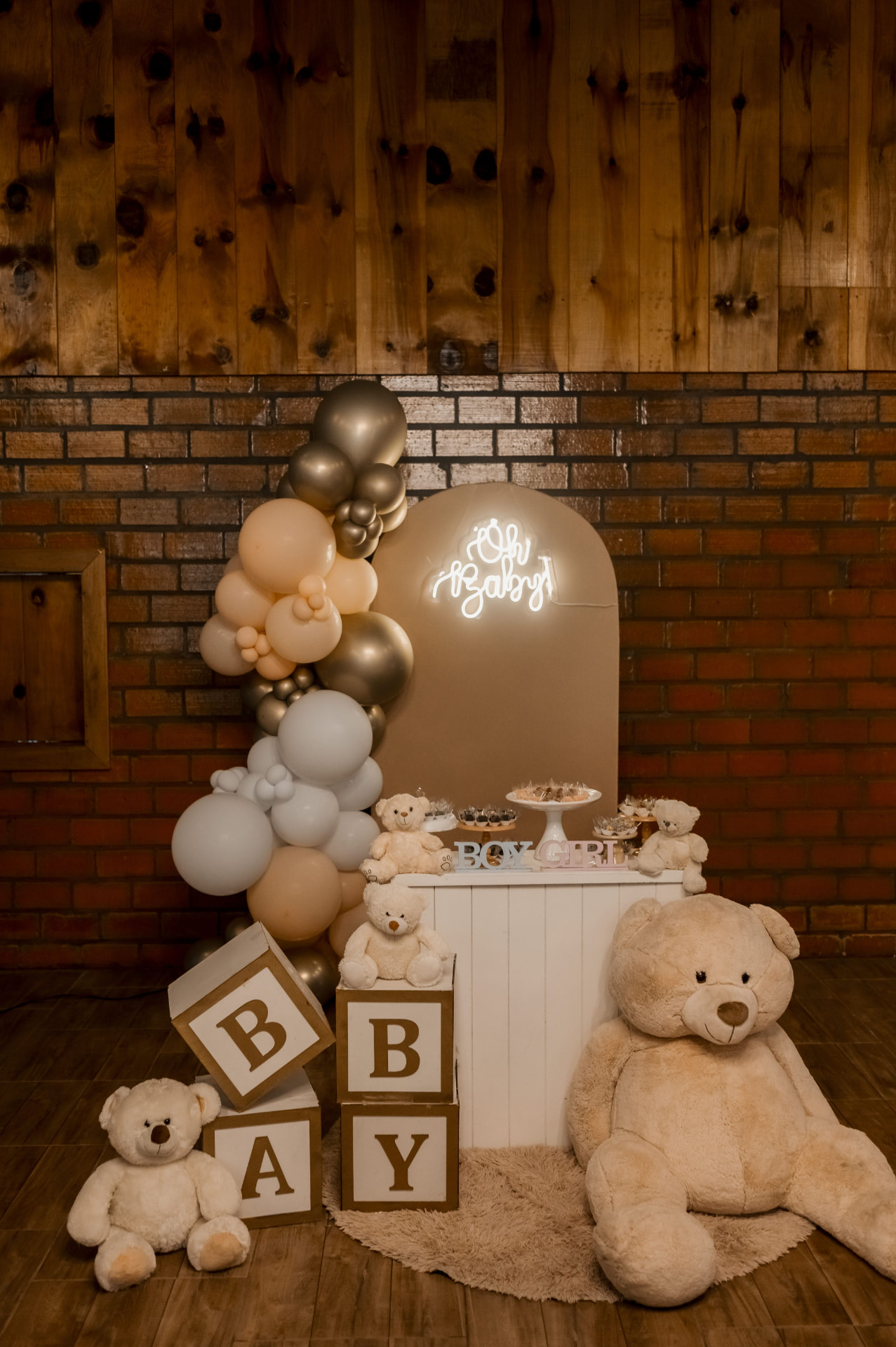 Neutral arched backdrop with an Oh Baby neon sign, nude, white and chrome balloon garland, teddy bears and baby blocks
