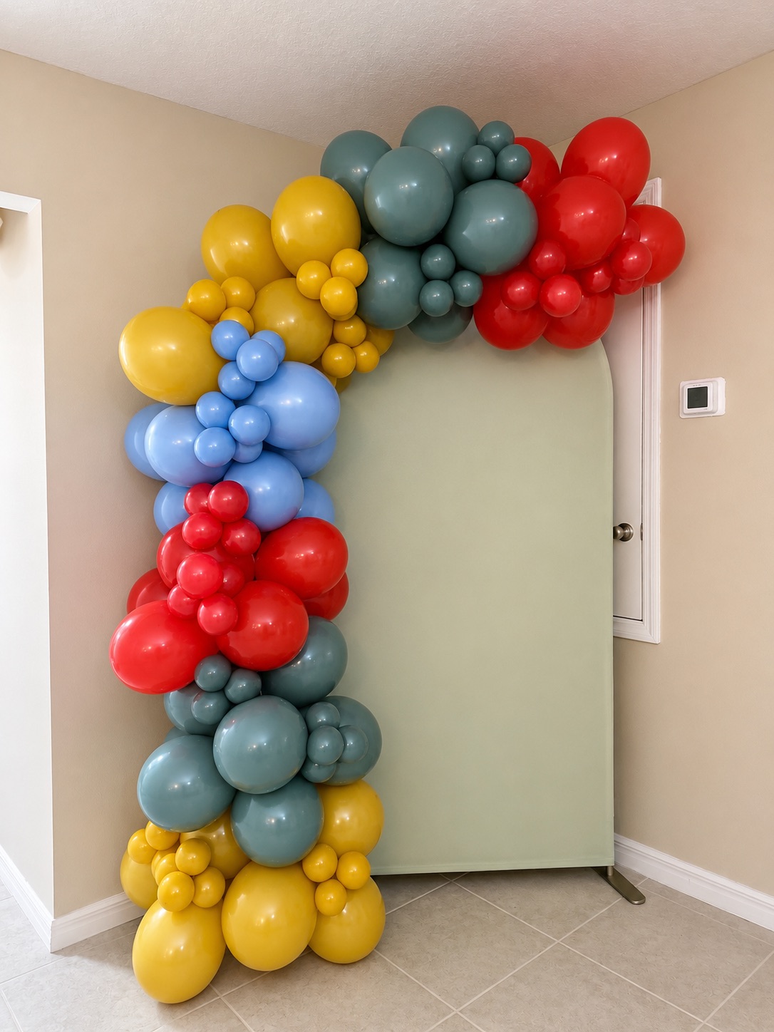 Sage arch panel with a bold balloon garland in red, mustard, light blue and slate grey